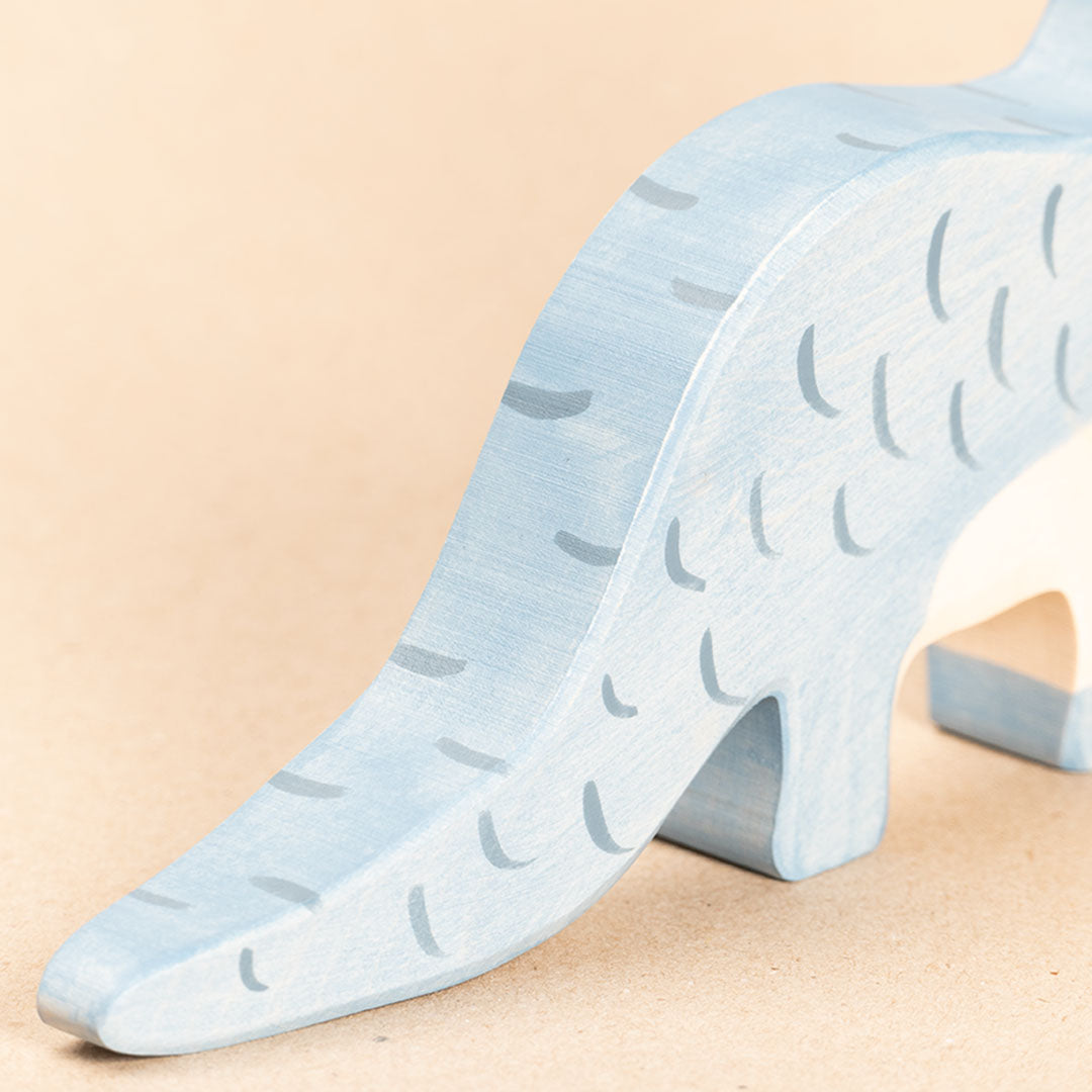 Brontosaurus aus Holz. Blau bemalt mit dunkelblauen Strichen. Nahaufnahme des Schweifes