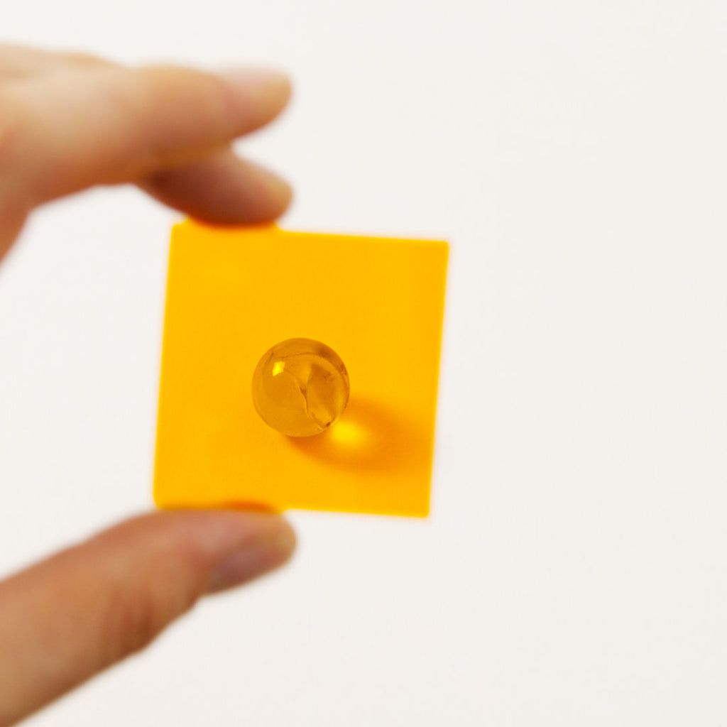 Farbplättchen aus transparenter Folie in Orange vor Murmel