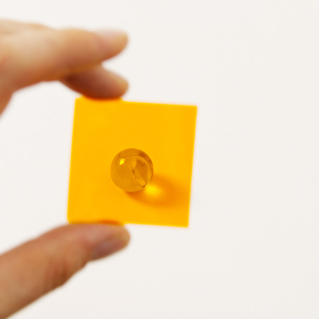 Farbplättchen aus transparenter Folie in Orange vor Murmel