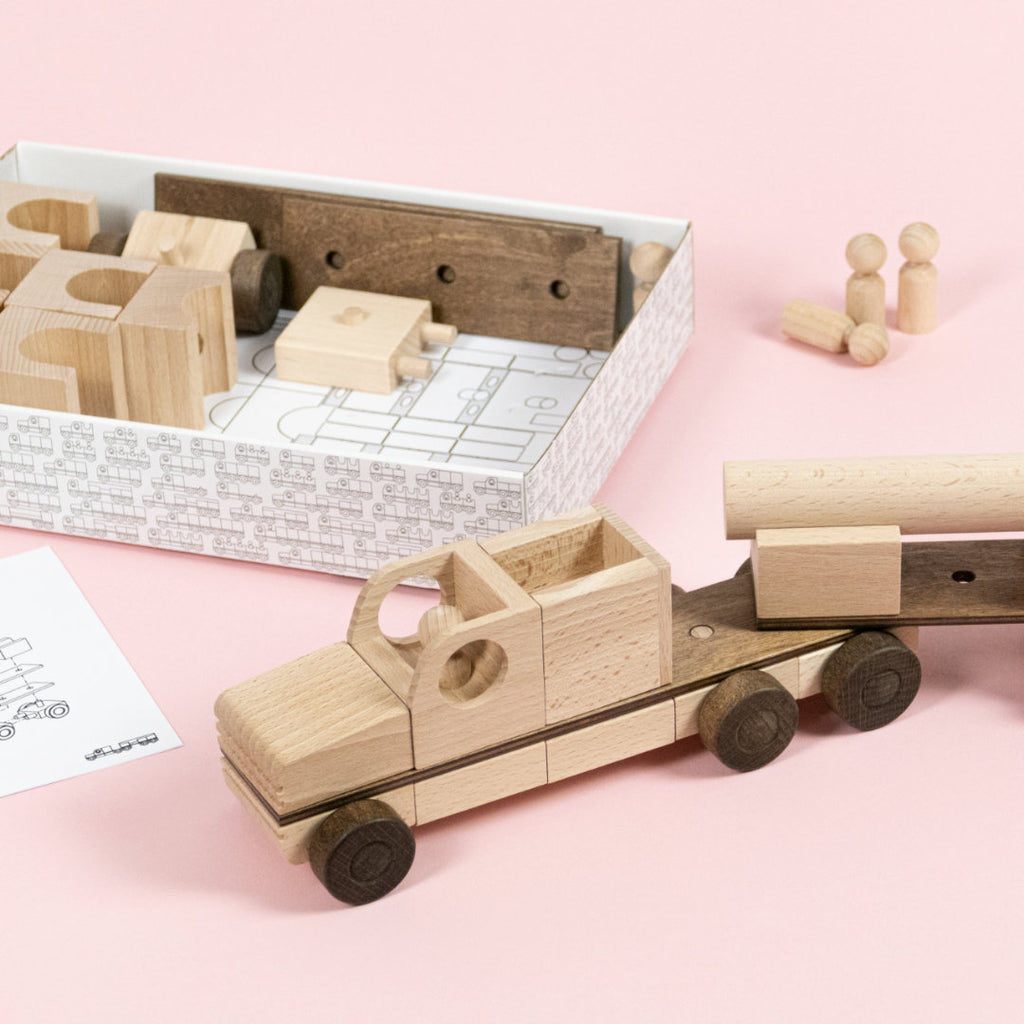 Holzelemente die zu einem Truck zusammengebaut sind, weitere Bauteile mit Bauanleitung aus Papier in einem Karton.