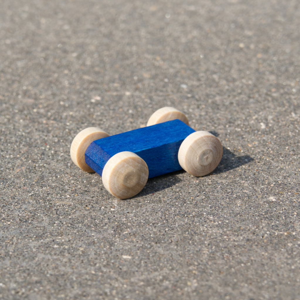 Kleines, leuchtend blaues, reduziertes Holzfahrzeug mit naturfarbenen Holzreifen, fahrbar