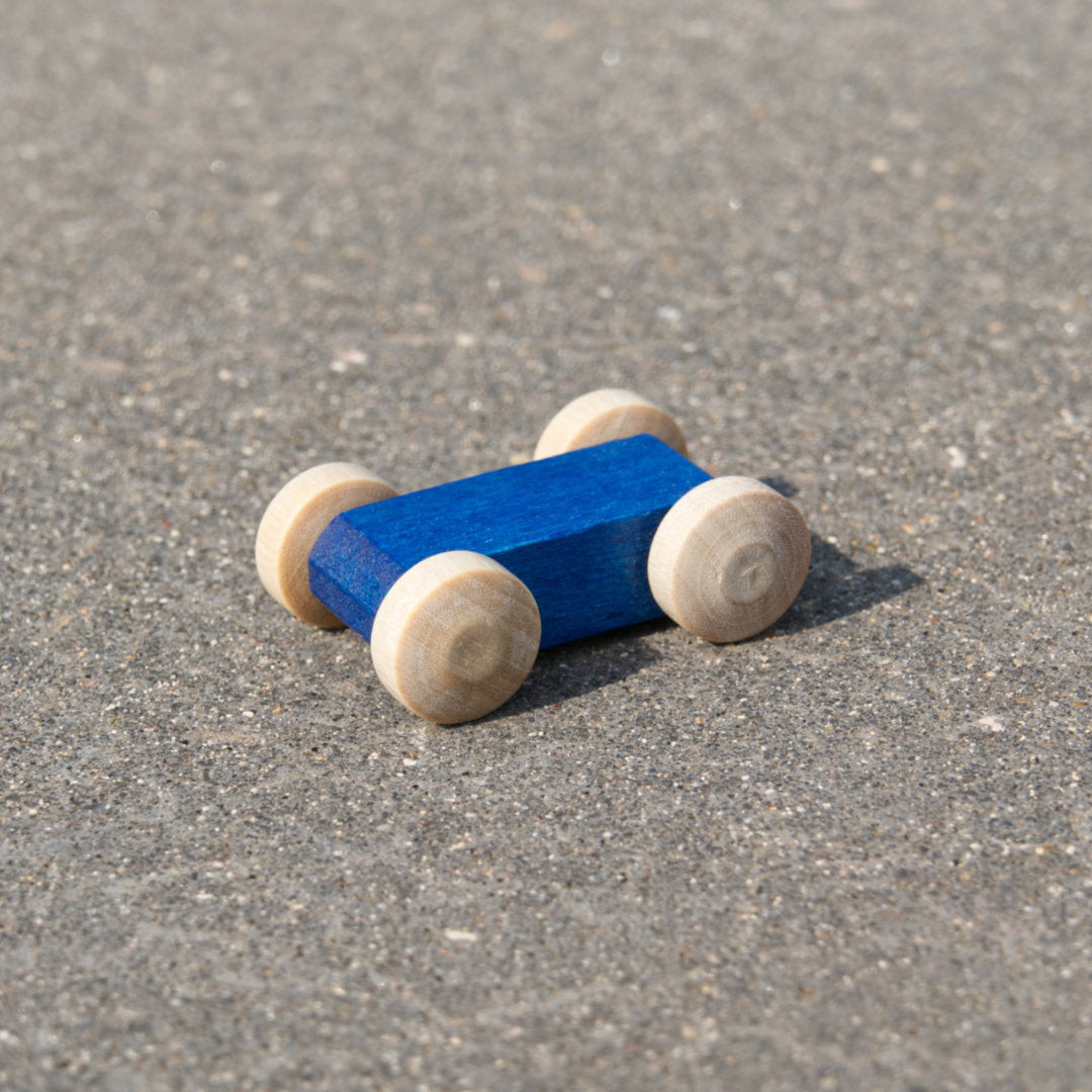 Kleines, leuchtend blaues, reduziertes Holzfahrzeug mit naturfarbenen Holzreifen, fahrbar