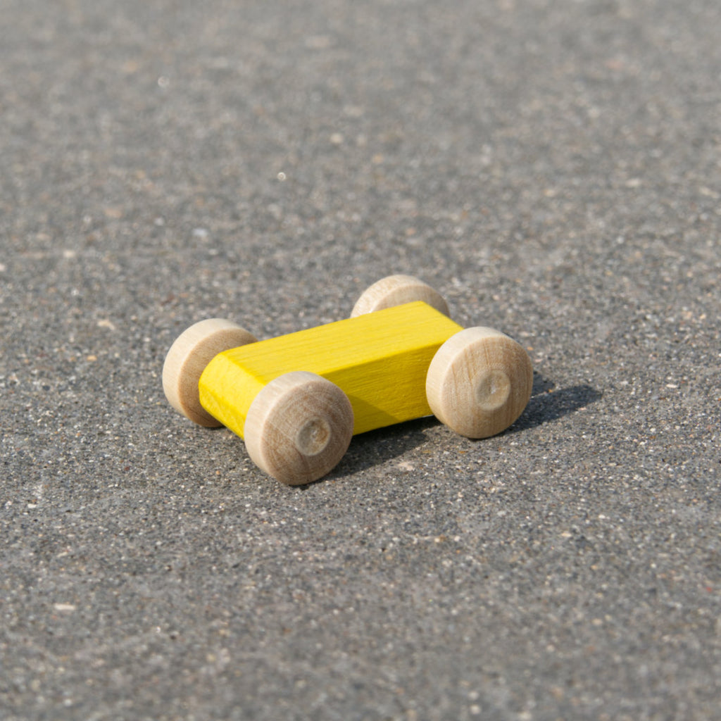 Kleines, leuchtend gelbes, reduziertes Holzfahrzeug mit naturfarbenen Holzreifen, fahrbar