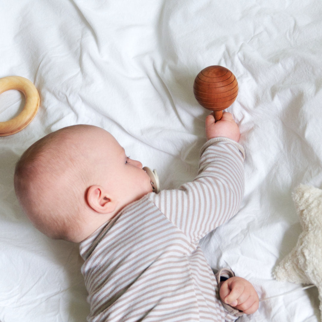 Baby liegt im Bett und spielt mit der Kugelrassel
