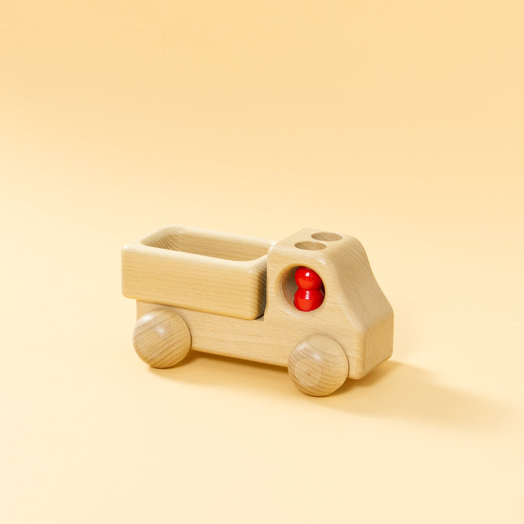 Lieferwagen aus Buchenholz, natur, mit abgerundeter Formensprache. Offene Ladefläche, Fahrerkabine mit zwei kegelförmigen, roten Figuren.