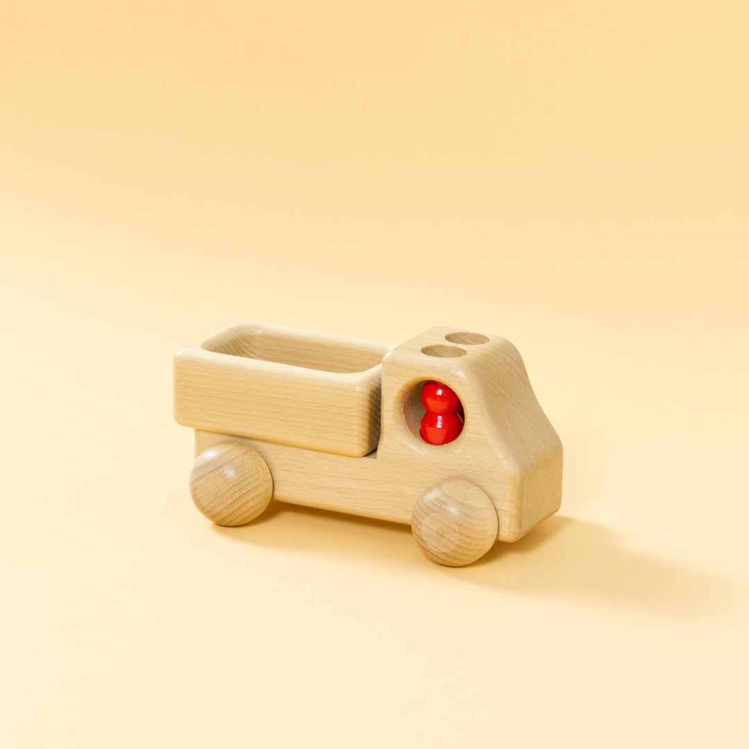 Lieferwagen aus Buchenholz, natur, mit abgerundeter Formensprache. Offene Ladefläche, Fahrerkabine mit zwei kegelförmigen, roten Figuren.