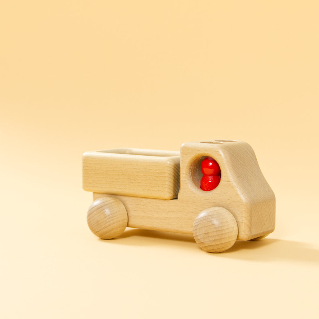 Lieferwagen aus Buchenholz, natur, mit abgerundeter Formensprache. Offene Ladefläche, Fahrerkabine mit zwei kegelförmigen, roten Figuren.