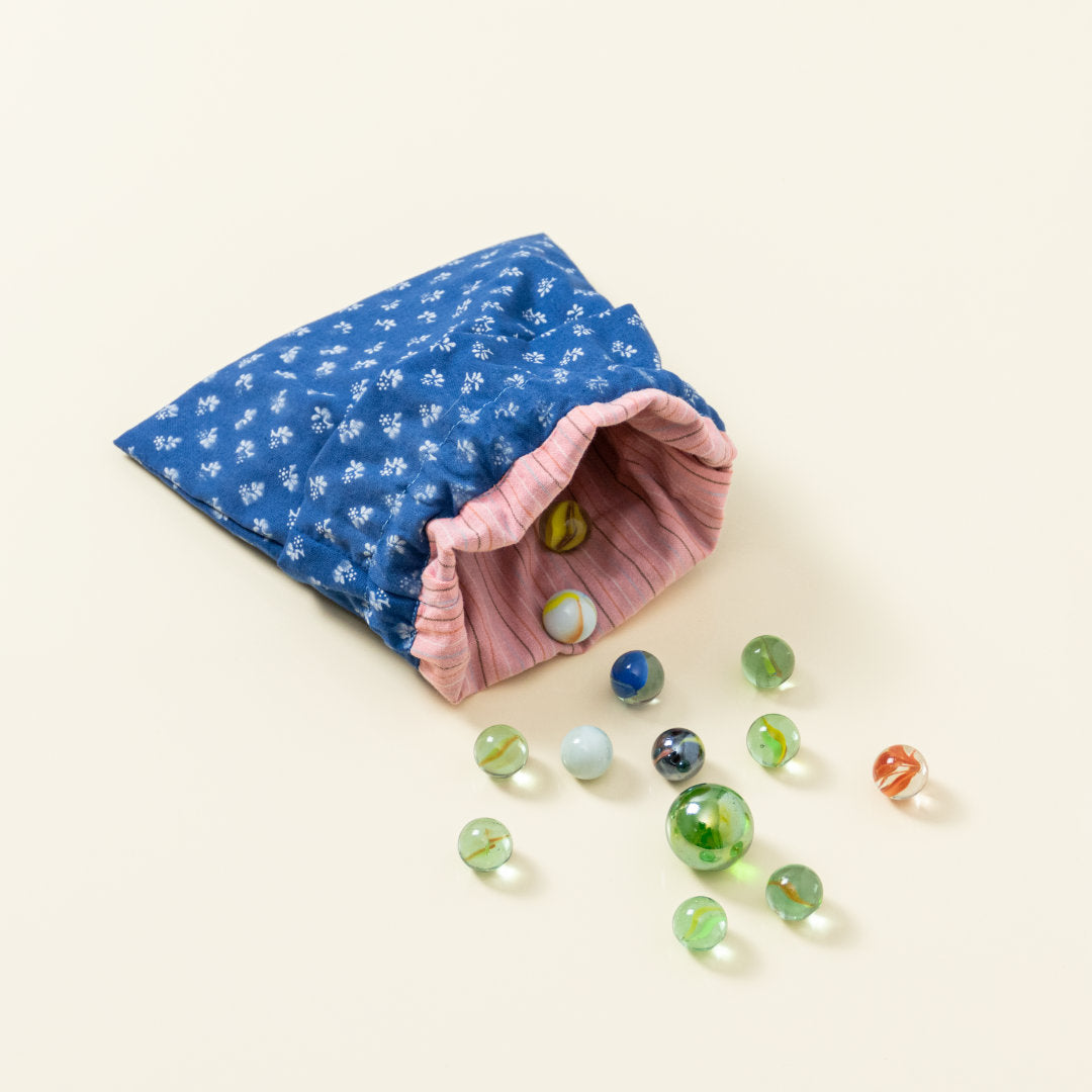 Hand-genähtes Murmelsäckchen mit Blumen-Muster in Blau-Weiß außen und rosa gestreift innen, geöffnet, inklusive einem individuellem Set aus einer großen Glas-Murmel und zwölf kleinen Glas-Murmeln