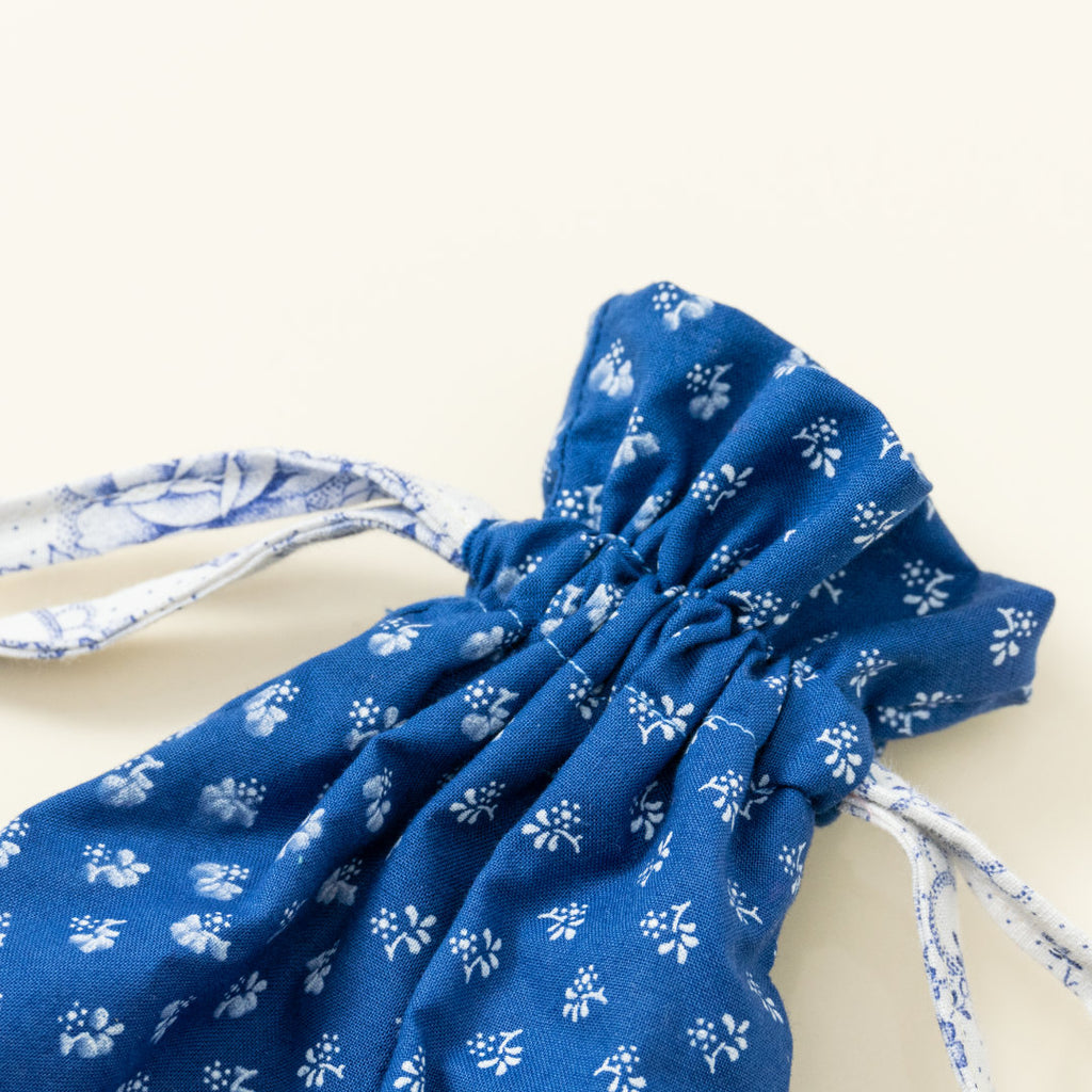 Hand-genähtes Murmelsäckchen mit Blumen-Muster in Blau-Weiß außen und rosa gestreift innen, geschlossen, inklusive einem individuellem Set aus einer großen Glas-Murmel und zwölf kleinen Glas-Murmeln, Detailaufnahme Bund Säckchen