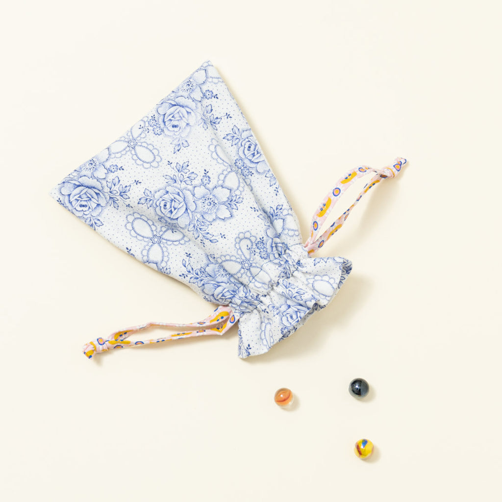 Hand-genähtes Murmelsäckchen mit Blumen-Muster in Weiß-Blau außen und gepunktet innen, geschlossen, inklusive einem individuellem Set aus einer großen Glas-Murmel und zwölf kleinen Glas-Murmeln