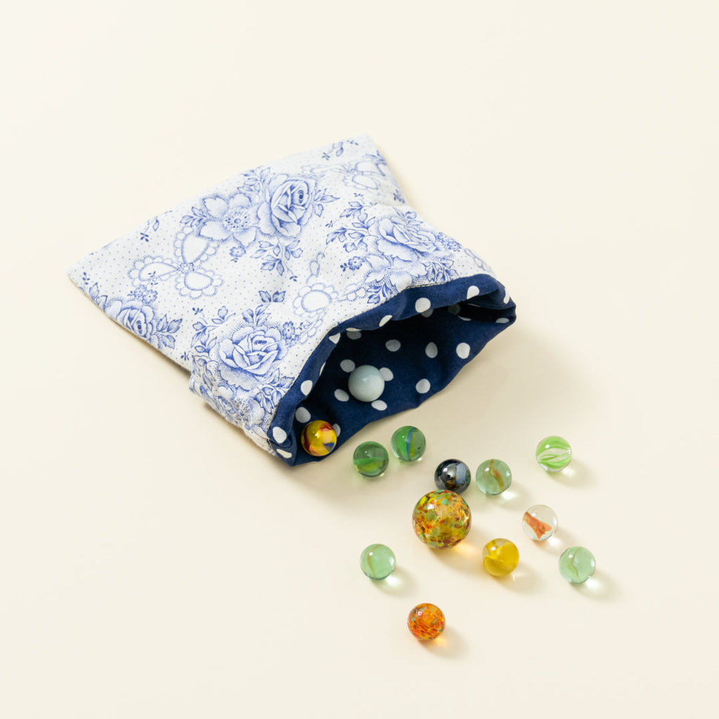 Hand-genähtes Murmelsäckchen mit Blumen-Muster in Weiß-Blau außen und gepunktet innen, geöffnet, inklusive einem individuellem Set aus einer großen Glas-Murmel und zwölf kleinen Glas-Murmeln