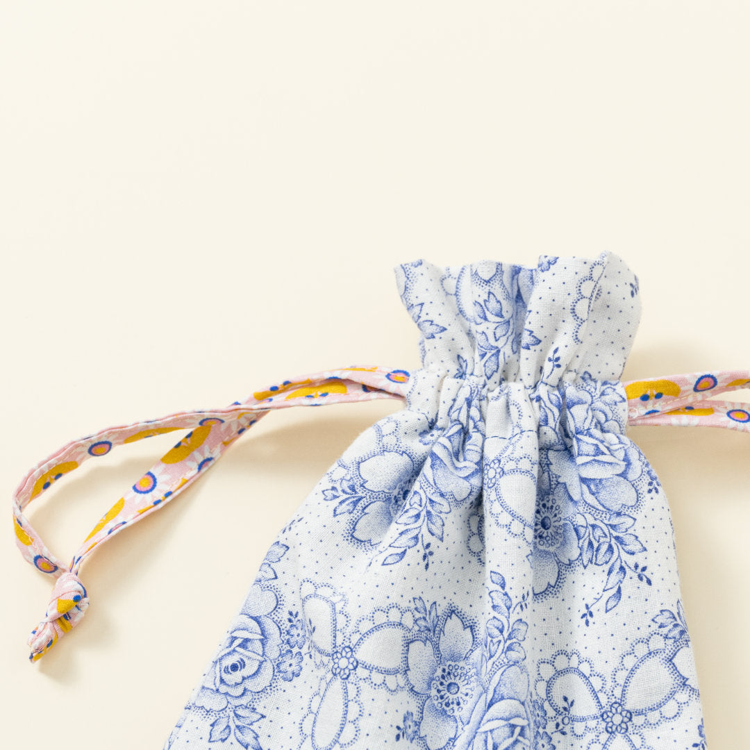Hand-genähtes Murmelsäckchen mit Blumen-Muster in Weiß-Blau außen und gepunktet innen, geschlossen, inklusive einem individuellem Set aus einer großen Glas-Murmel und zwölf kleinen Glas-Murmeln, Detailaufnahme Bund Säckchen