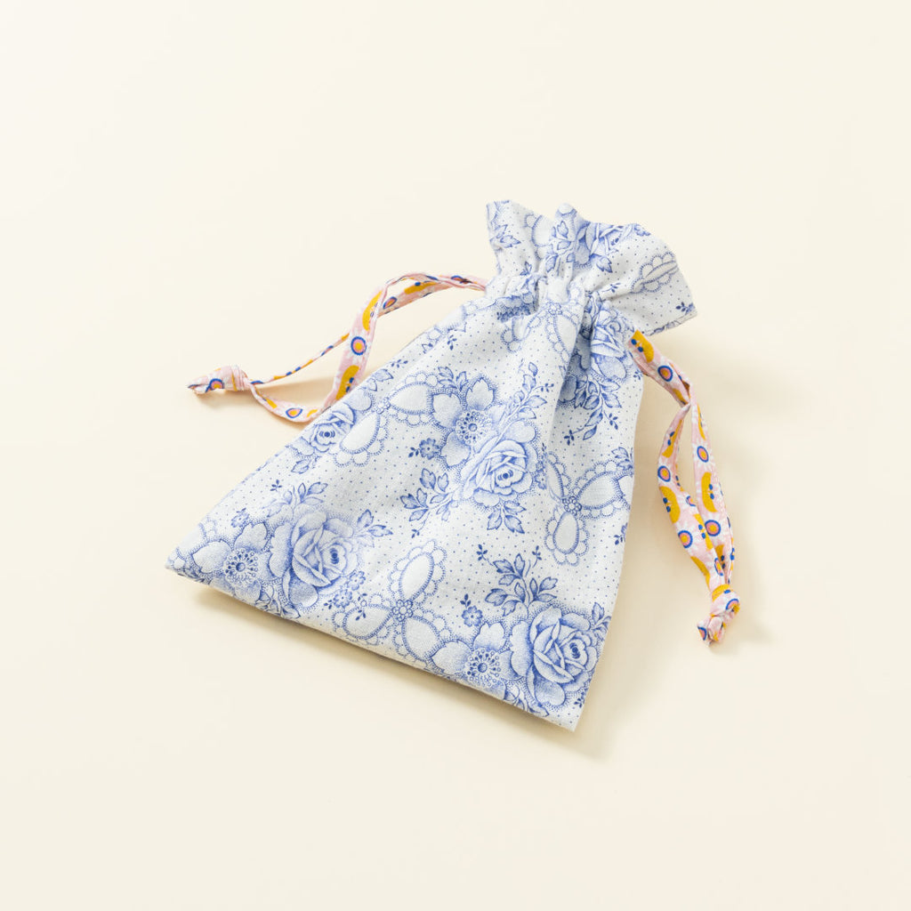 Hand-genähtes Murmelsäckchen mit Blumen-Muster in Weiß-Blau außen und gepunktet innen, geschlossen, inklusive einem individuellem Set aus einer großen Glas-Murmel und zwölf kleinen Glas-Murmeln