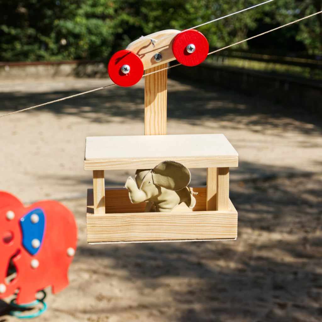 Bausatz für eine Seilbahn aus Natur-Holz mit Passagiergondel, aufgebaut mit Elefant-Figur als Passagier