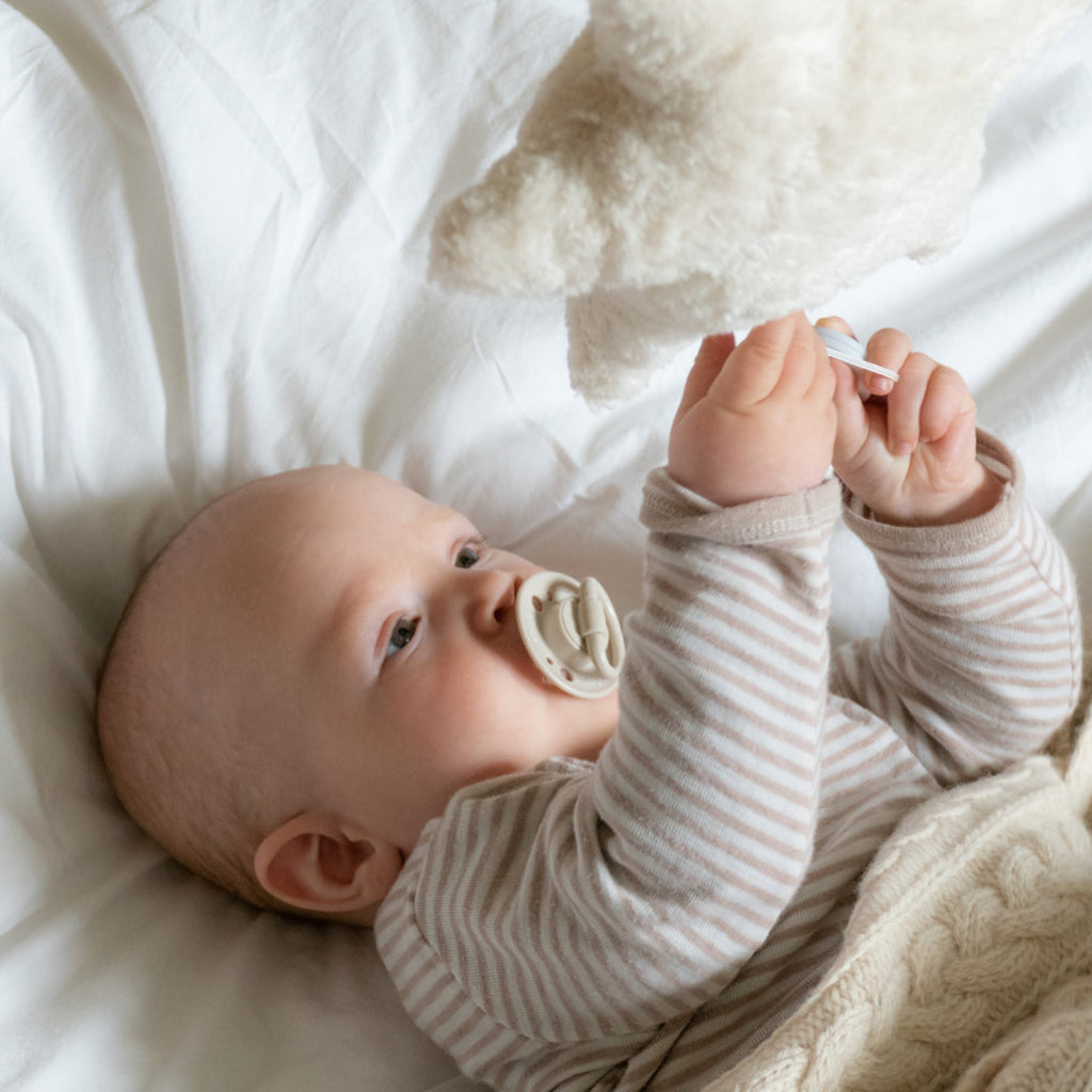 Baby spielt mit weißem Bio-Kuscheltier in Sternform, aus Schafwolle und integrierter Spieluhr