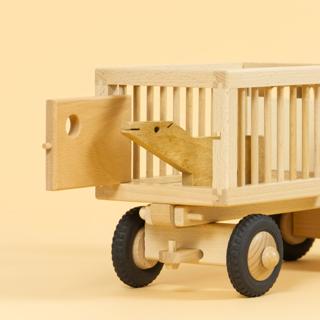 Holzfahrzeug Zirkuswagen für Tiere aus naturlackiertem Buchenholz und Reifen aus Vollgummi, Anhänger mit Gitterstäben an der Seite und geöffneter Tür hinten, Tier schaut hinaus