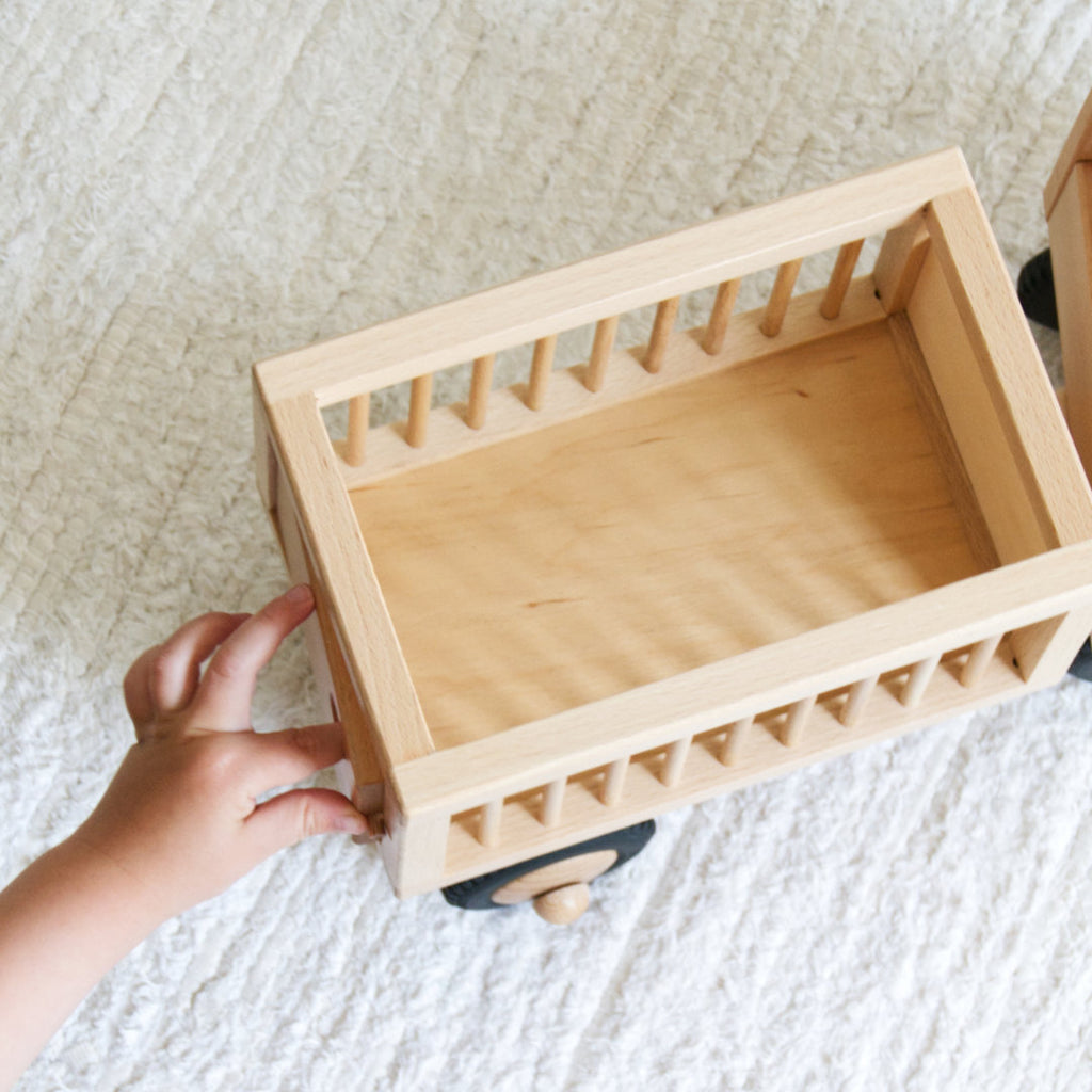 Kleinkind spielt mit Holz-Fahrzeug Typ Zirkuswagen