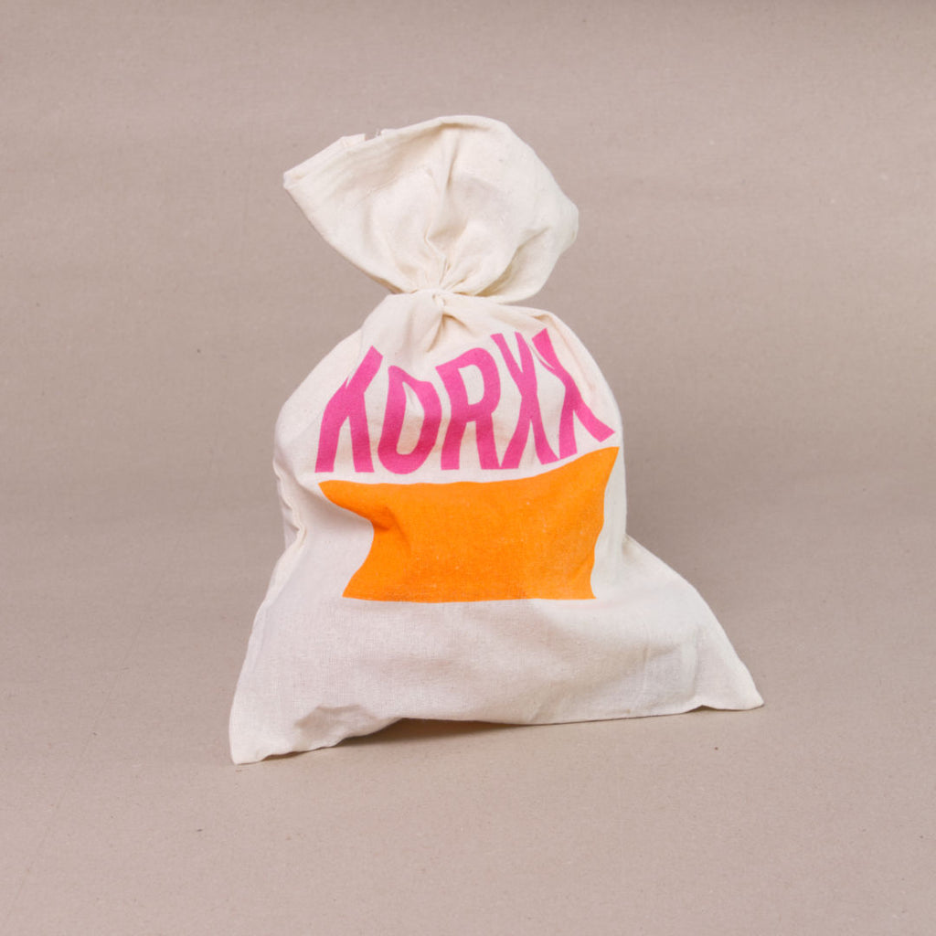 Jutebeutel in naturfarben als Verpackung für das 3er-Kugel-SetC von Korxx mit rosa, orangenem Aufdruck.