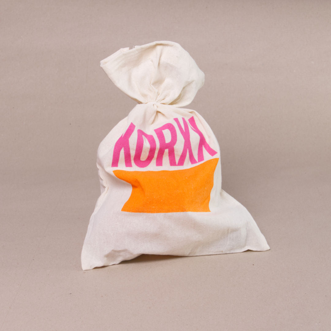 Jutebeutel in naturfarben als Verpackung für das 3er-Kugel-SetC von Korxx mit rosa, orangenem Aufdruck.