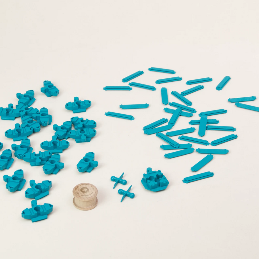 Zu sehen sind alle Elemente des Adapter-Sets Helix 3 von Yamba: insgesamt 57 türkise Bausteine in vier unterschiedlichen Formen – Verbindungsstück LinkUp, Verbindungsknochen Bar, Verbindungsstück Cross und Säule Lift. Die Einzelteile bestehen aus hochwertigem ABS-Kunststoff und sind im Spritzgussverfahren hergestellt. Zusätzlich enthält das Set einen Rolli, eine zylindrische Holzwalze.