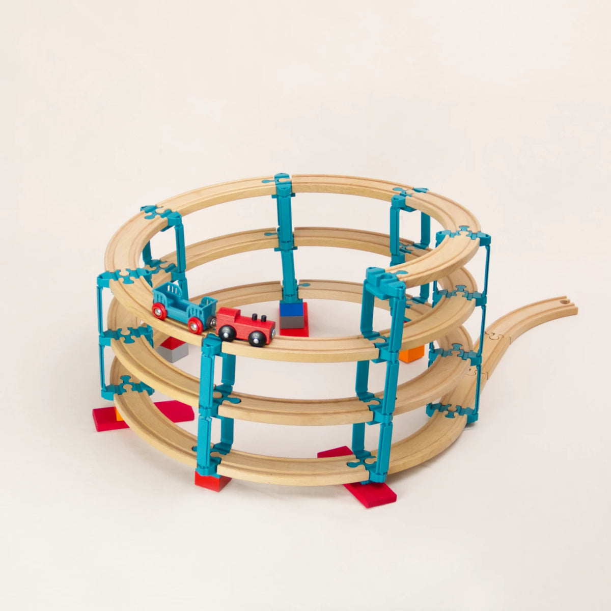 Das Adapter-Set Helix 3 von Yamba ermöglicht, Klemmbausteine (DUPLO®, BioBUDDi®, Hubelino® usw.) und Schienen (BRIO®, IKEA®, Eichhorn®, Hape® usw.) zu einem Säulensystem mit bis zu vier Etagen zu verbinden. Auf der Bahn fährt eine rote Holzlokomotive nach unten, an der ein türkisfarbener Wagen hängt.