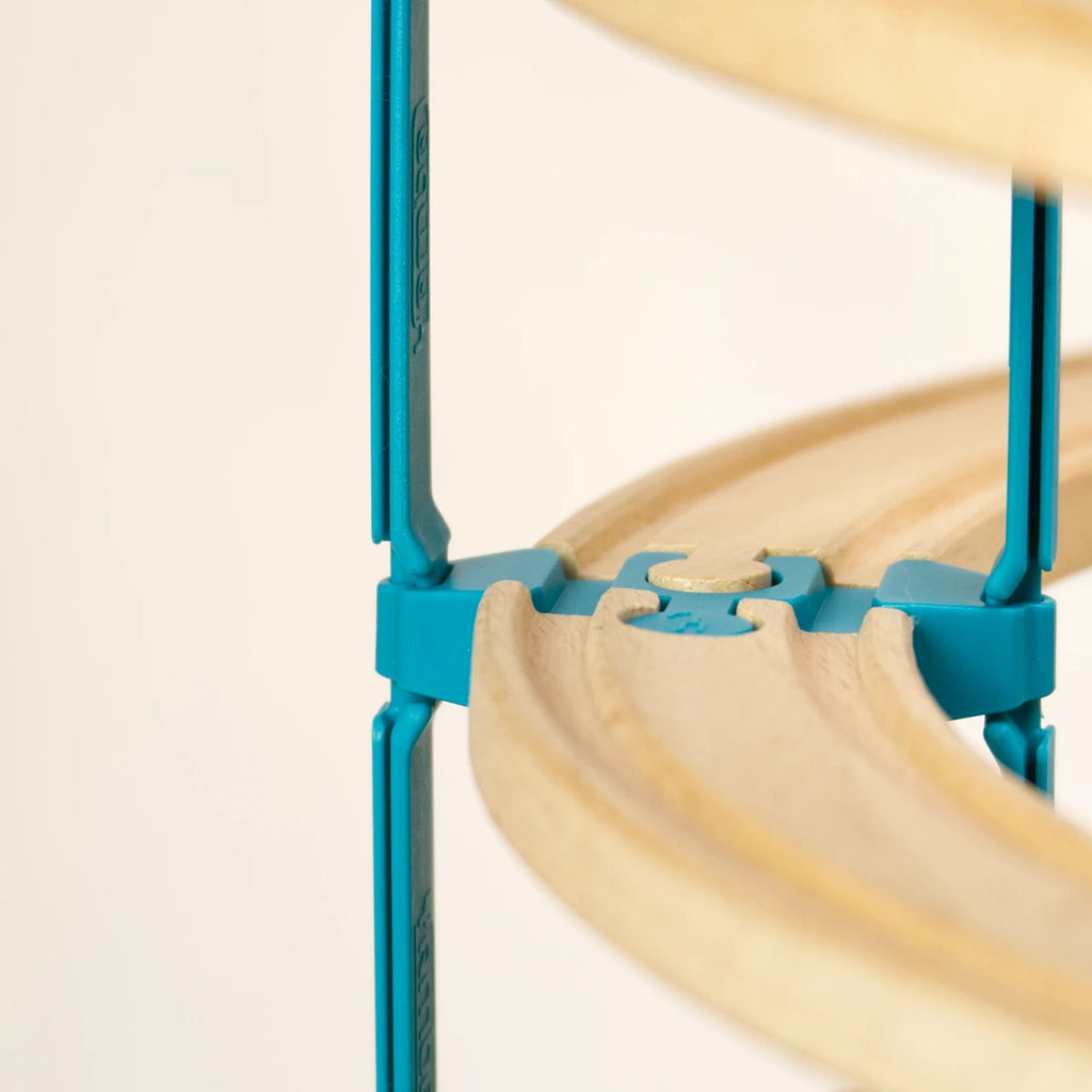 Das Adapter-Set Helix 3 von Yamba ist in einem Detailausschnitt aufgebaut zu sehen. Zwei Holzschienen sind durch ein Verbindungsstück LinkUp verbunden. Seitlich davon führen zwei Säulenelemente Lift jeweils nach oben und unten. So lassen sich mehrere Stockwerke der Bahn übereinander aufbauen.