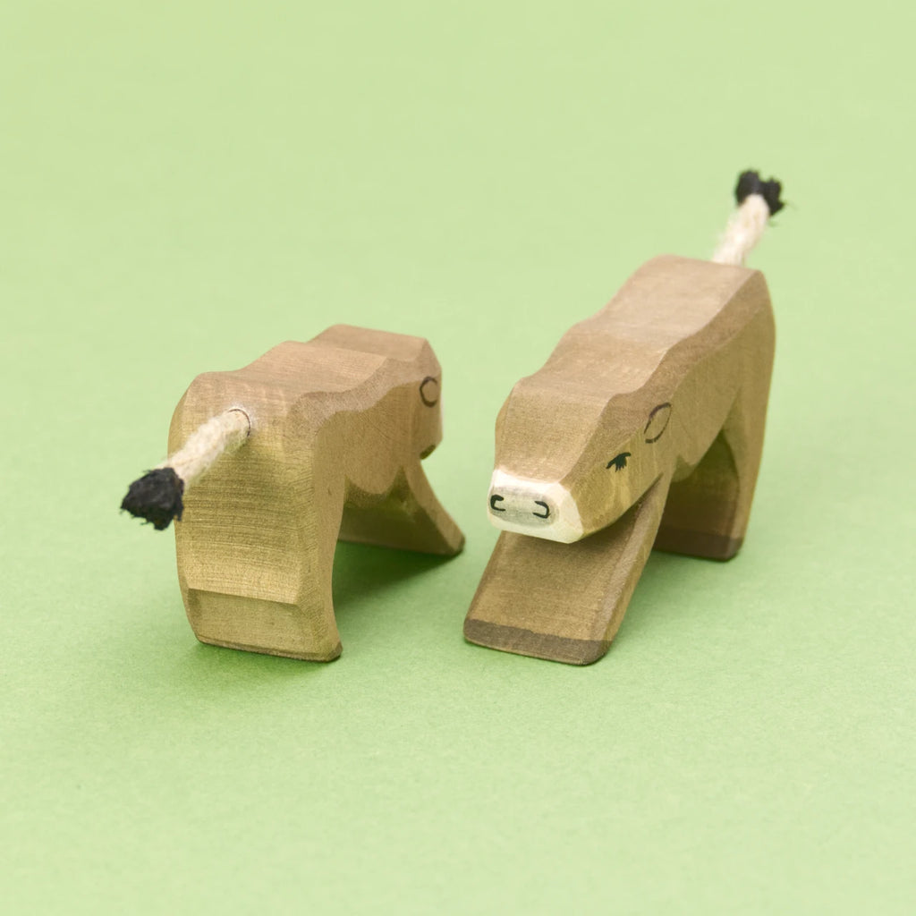 Zwei hölzerne Kälbchen, Spieltiere der Marke Ostheimer. Beide Kälber stehen parallel zueinander; eins blickt nach vorne, das andere nach hinten. Das Bild verdeutlicht, dass es sich um flach ausgesägte Figuren handelt. Das Kalb eine gebeugte Position zum trinken, die Kanten sind leicht abgerundet.Das Fell ist braun und die Schnauze ist weiß. Der Schwanz ist eine weiße Kordel mit schwarzer Spitze.