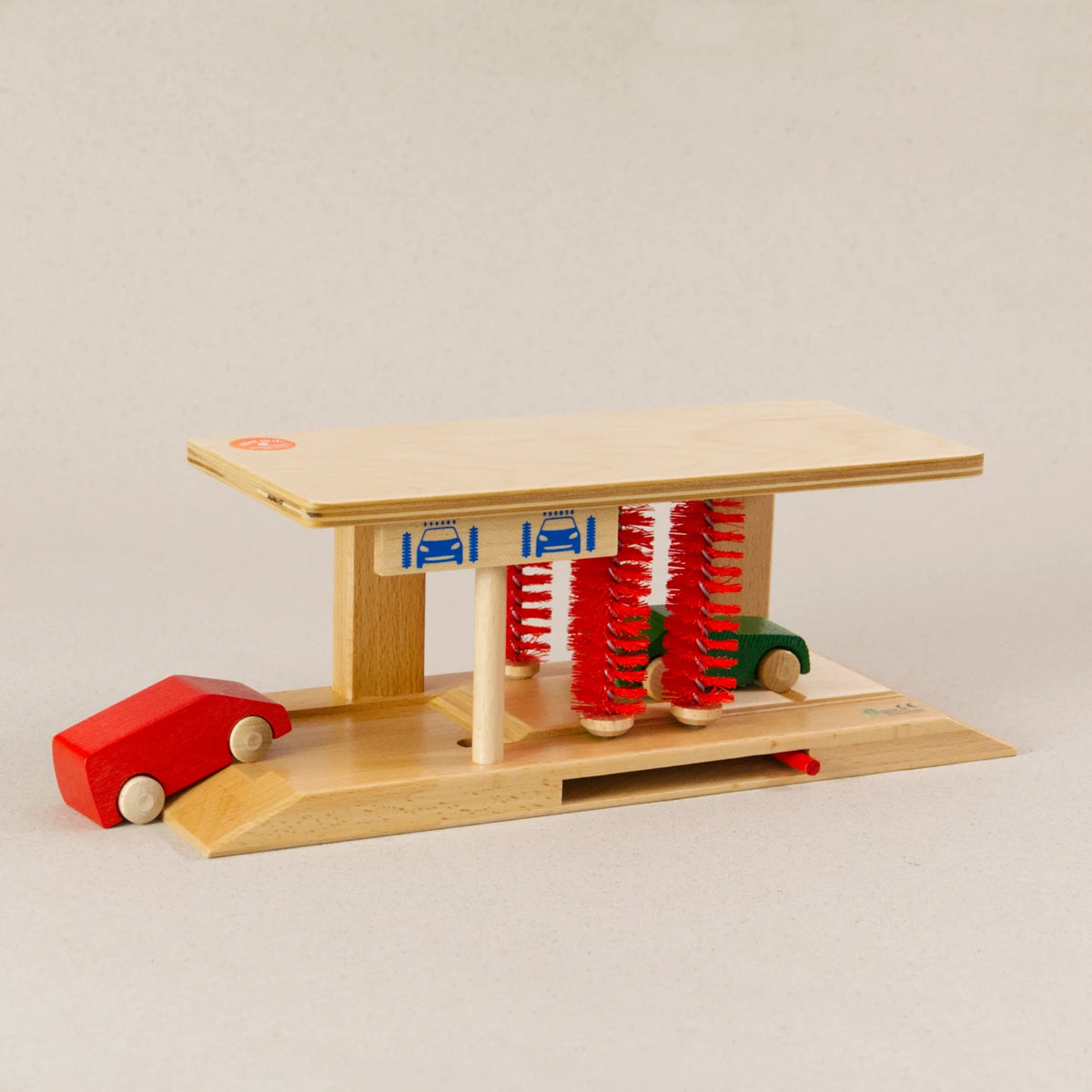 Waschanlage von Beck aus Holz. Die vier Bürsten sind in rot. Ein grünes und rotes Auto fahren durch.