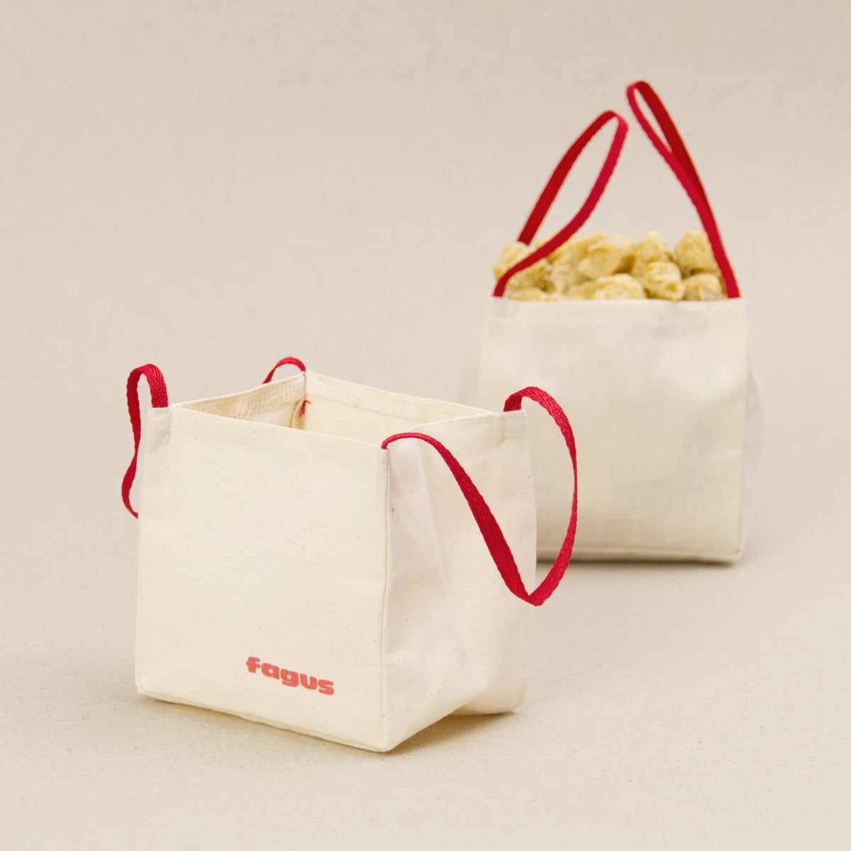 Zwei Big Bags von fagus aus heller Baumwolle mit jeweils zwei roten Trageschlaufen. Der eine Big Bag ist mit Schüttmaterial gefüllt. Sie haben das fagus Logo in rot auf der Vorderseite aufgedruckt.