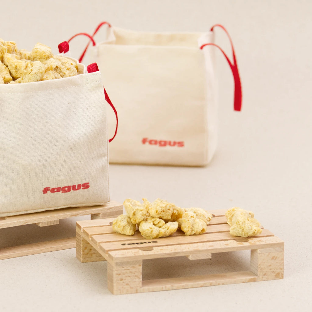 Zwei Big Bags von fagus aus heller Baumwolle mit jeweils zwei roten Trageschlaufen. Der eine Big Bag ist mit Schüttmaterial gefüllt und steht auf einer fagus Europlatte. Eine weitere Europlatte steht daneben, auch auf ihr ist Schüttmaterial.
