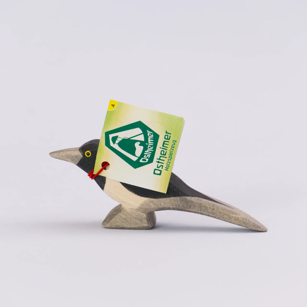 Elster von Ostheimer aus Holz zum Spielen. In den Farben Schwarz, Grau, Weiß und Gelb für die Augen. Seitenansicht, mit Verpackungszettel.