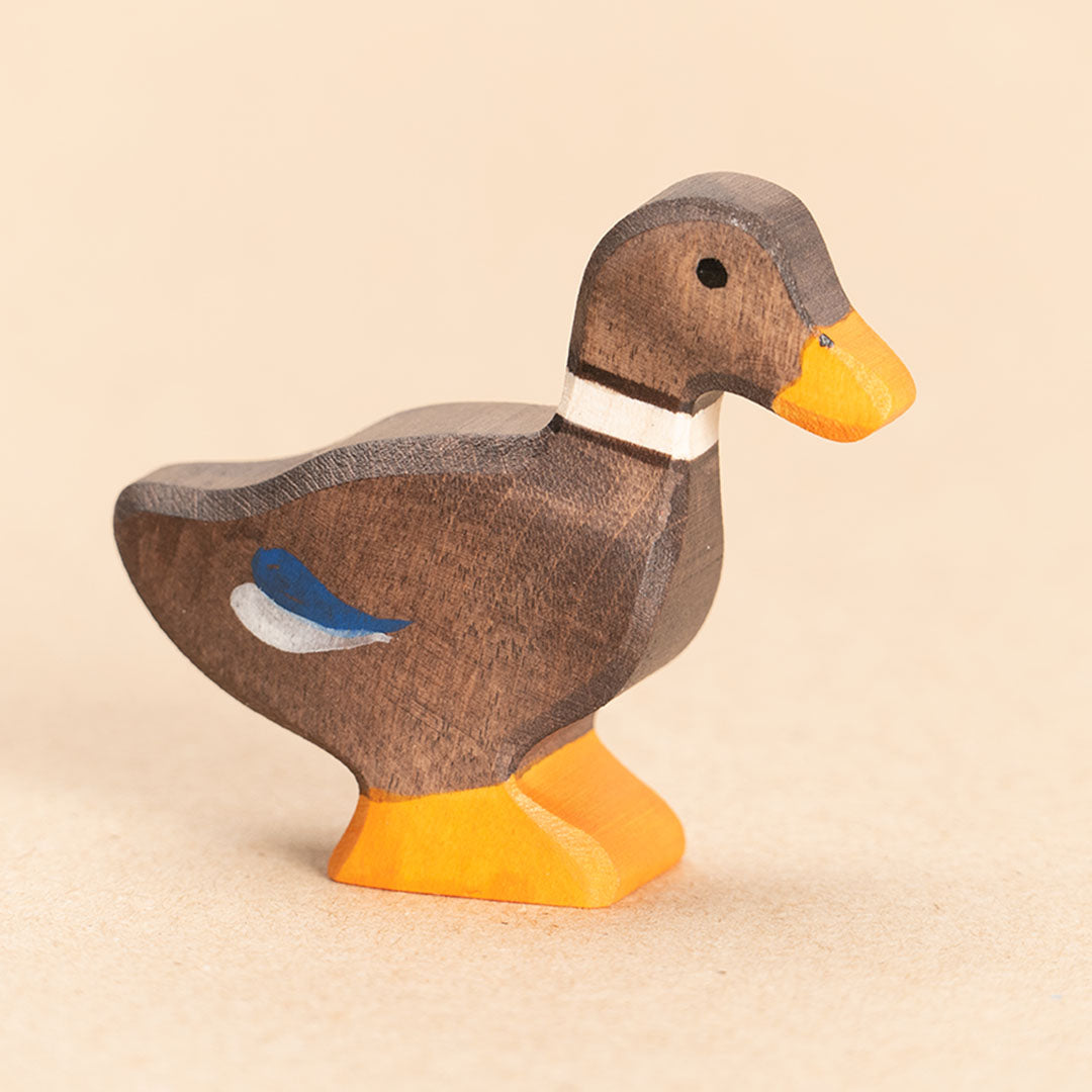Ente aus Holz. Braun bemalt mit blauen Federakzenten und orangenem Schnabel und Entenpaddel. Nahaufnahme