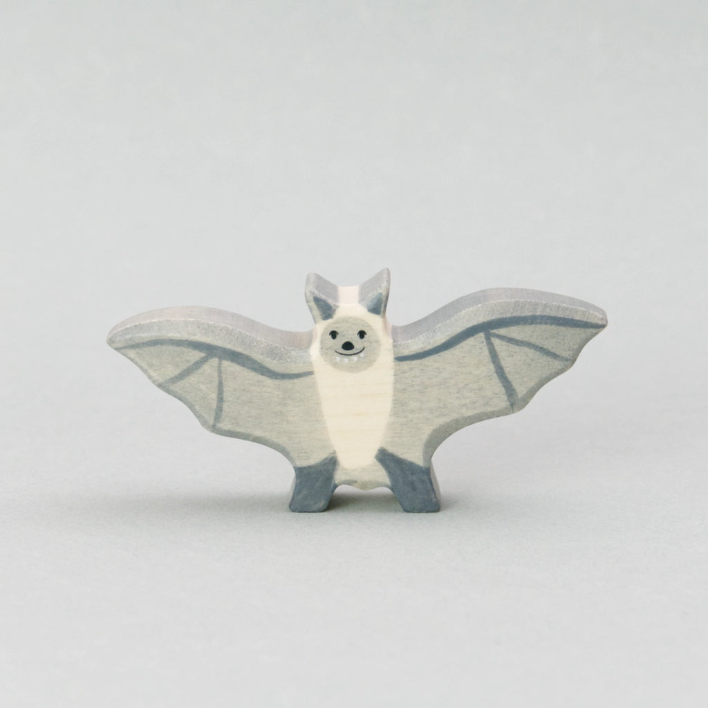 Handgefertigte Fledermaus Holztiger Figur aus naturbelassenem Holz. Die Fledermaus hat ausgebreitete graue Flügel mit feinen dunkleren Linien, einen cremefarbenen Körper und ein freundliches Gesicht mit kleinen schwarzen Augen und einem dezenten Lächeln. Perfekt als Holztier Spielzeug für Kinder oder als stilvolle Halloween Deko