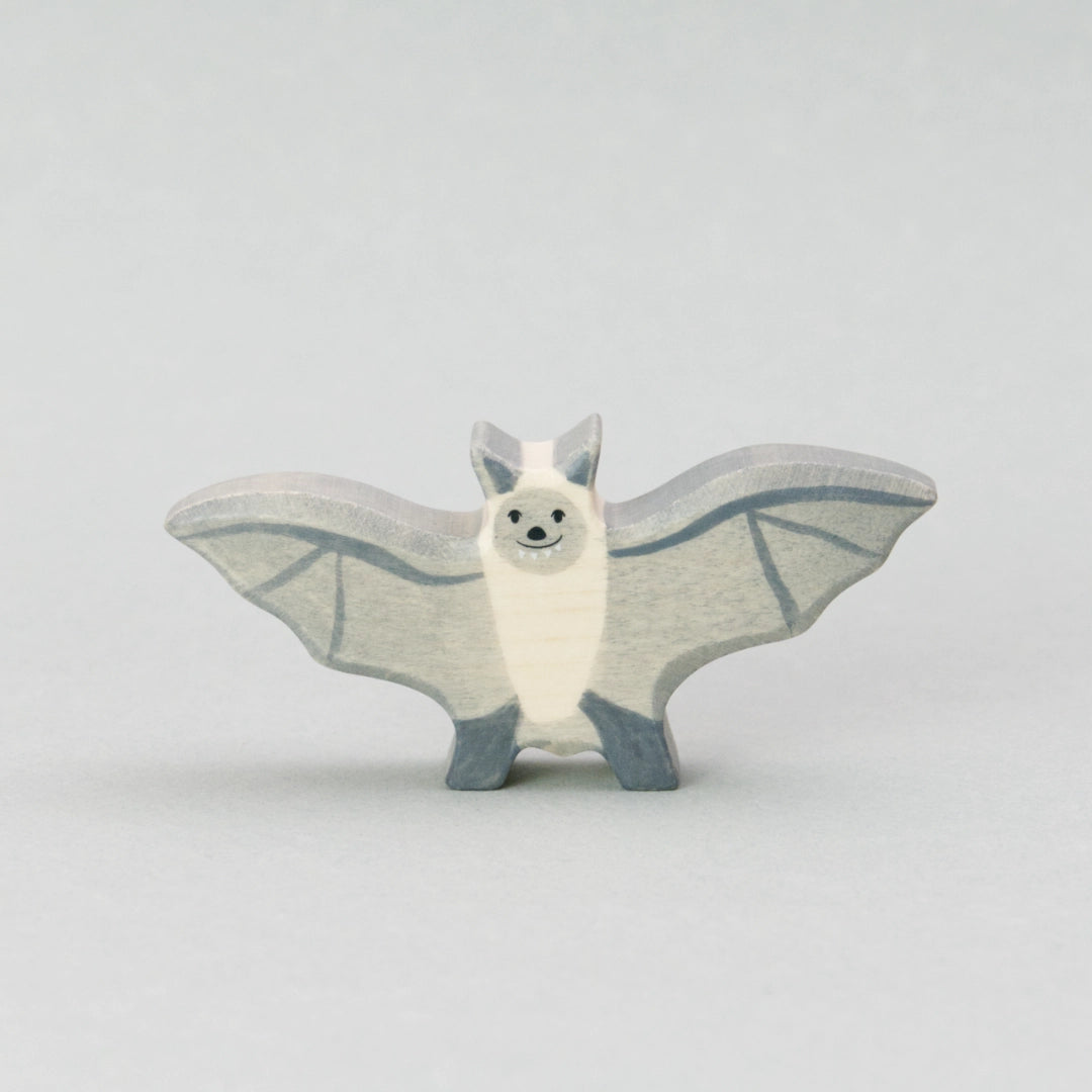 Handgefertigte Fledermaus Holztiger Figur aus naturbelassenem Holz. Die Fledermaus hat ausgebreitete graue Flügel mit feinen dunkleren Linien, einen cremefarbenen Körper und ein freundliches Gesicht mit kleinen schwarzen Augen und einem dezenten Lächeln. Perfekt als Holztier Spielzeug für Kinder oder als stilvolle Halloween Deko
