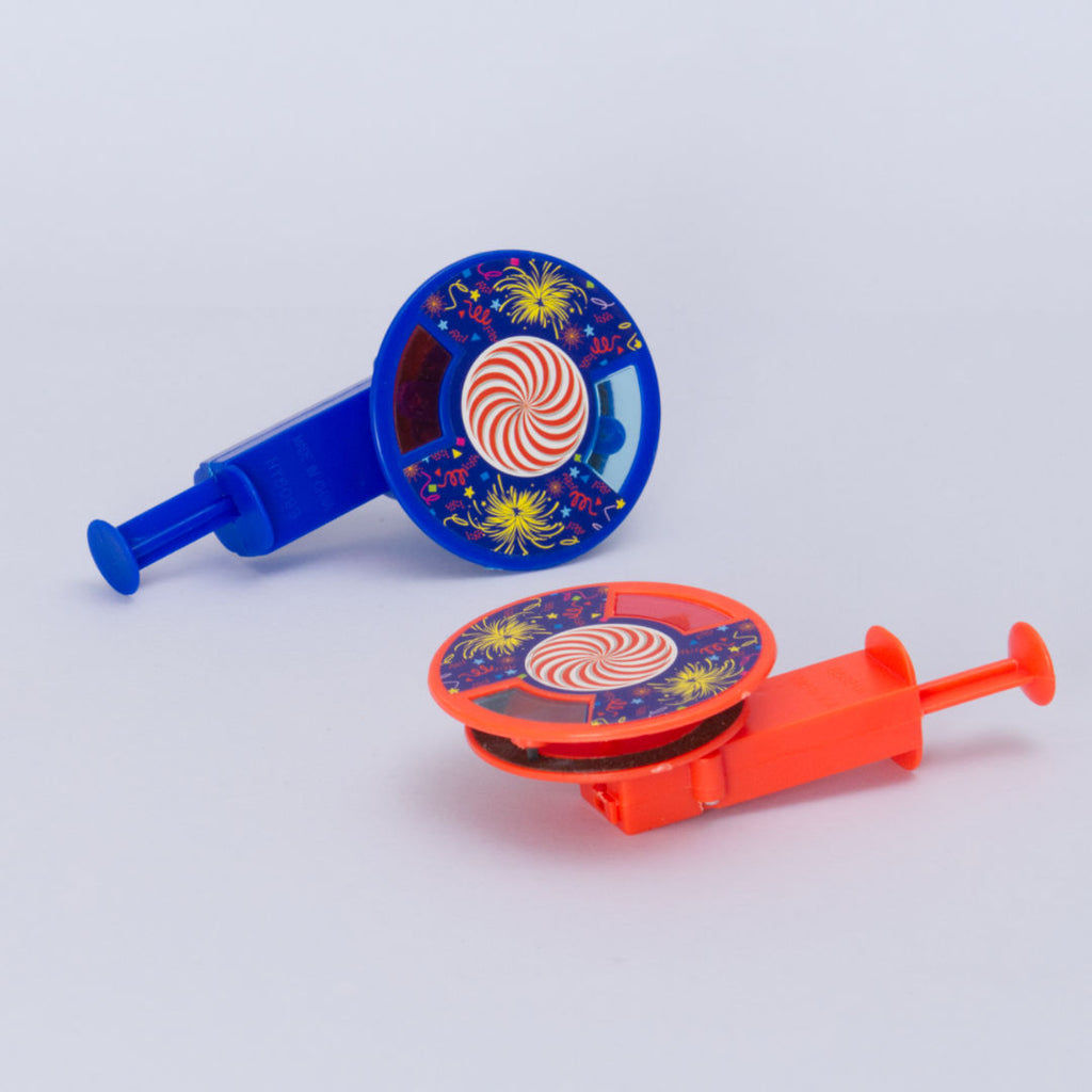 Die Funkenkreisel von Goki. Der vordere ist rot und liegt auf dem Rücken vor dem blauen Kreisel, der seitlich liegt. Beide haben ein buntes Feuerwerks Design auf der Kreiselfläche.