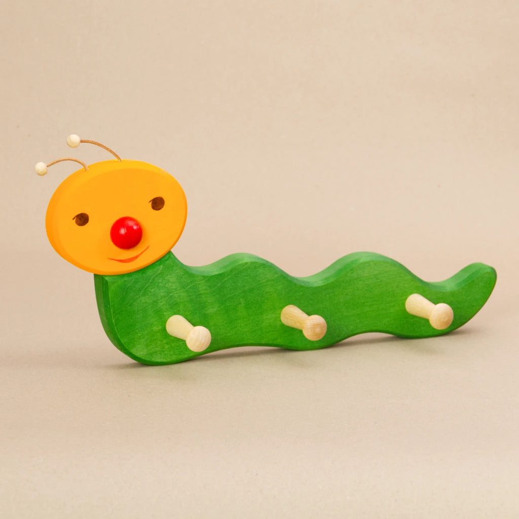 Ostheimer Kindergarderobe Wurm – handbemalte Garderobe aus Holz in geschwungener Wurmform, mit grünem Körper, gelbem Kopf, roter Nase und zwei Lederfühlern. Ideal zum Aufhängen von Kinderkleidung wie Jacken, Mützen und Taschen.