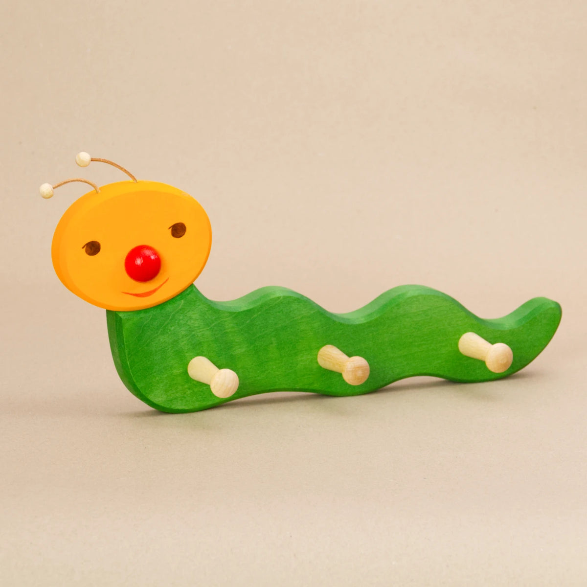 Ostheimer Kindergarderobe Wurm – handbemalte Garderobe aus Holz in geschwungener Wurmform, mit grünem Körper, gelbem Kopf, roter Nase und zwei Lederfühlern. Ideal zum Aufhängen von Kinderkleidung wie Jacken, Mützen und Taschen.
