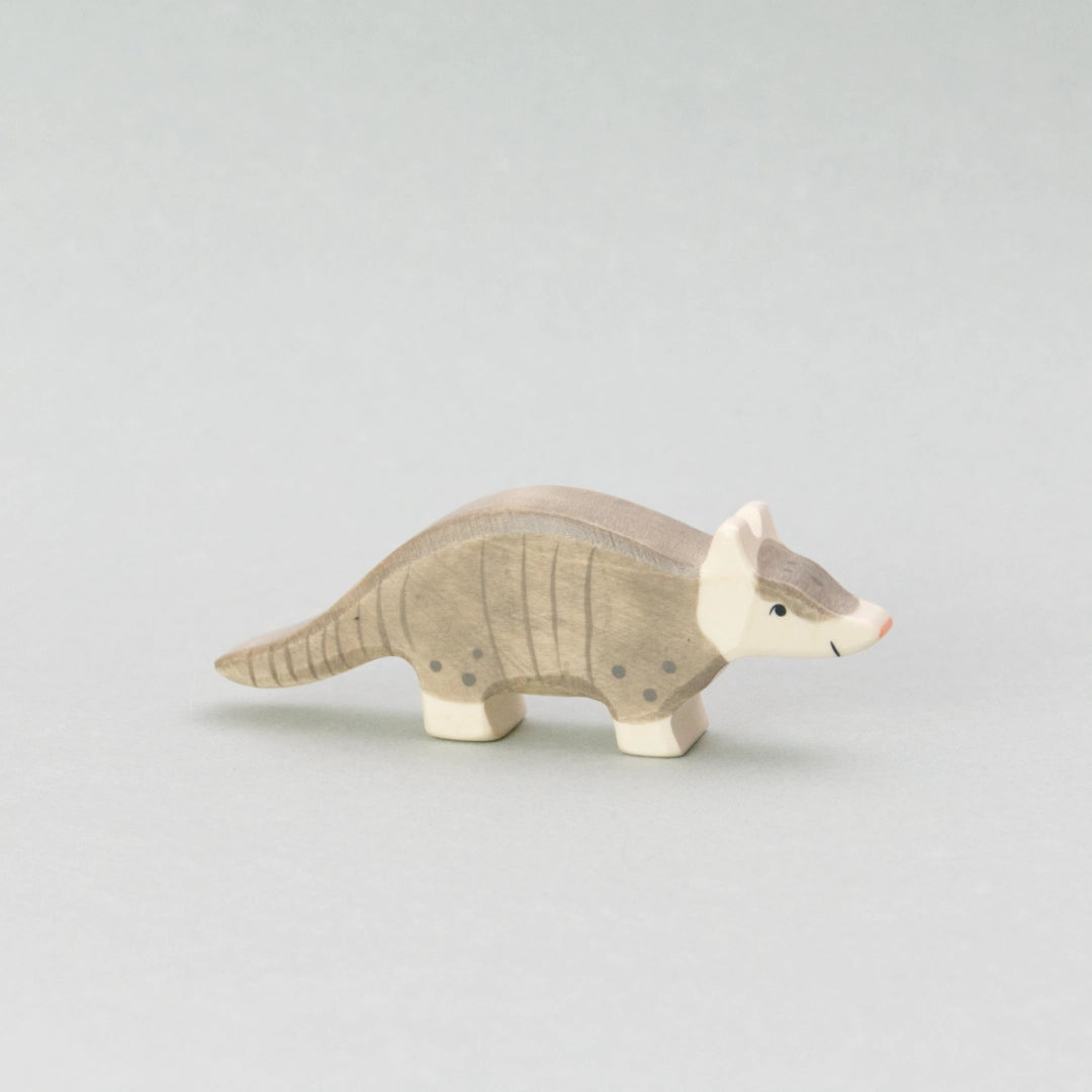Das Gürteltier von Holztiger ist eine detailreiche Holzfigur mit handbemalter Oberfläche. Das Spielzeug-Holztier hat einen grauen Körper mit aufgemalten Gürtellinien, die seinen typischen Panzer nachbilden. Der Kopf und die Beine sind in einem sanften Cremeweiß gehalten, während die kleine, spitz zulaufende Nase in einem zarten Rosa leuchtet. Die Figur hat eine geschwungene Körperhaltung und steht stabil auf vier Beinen – ideal für kreatives Spielen oder als dekorative Ergänzung in einer Tierwelt-Sammlung.