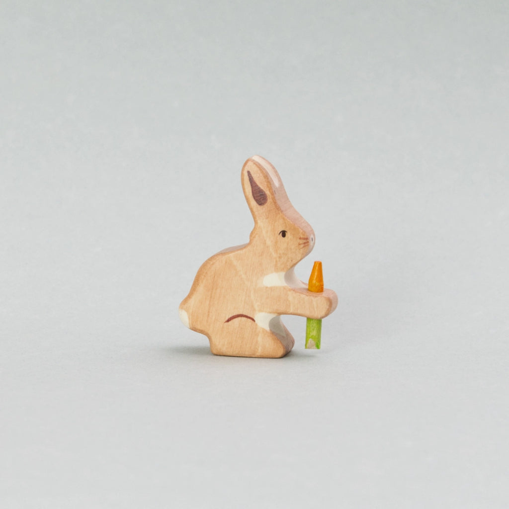 Diese handbemalte Holzfigur „Hase mit Karotte“ von Holztiger zeigt ein niedliches Holztier mit hellbraunem Fell und weißen Akzenten. Der kleine Hase hält eine leuchtend orangefarbene Karotte mit grünem Stiel fest in seinen Pfoten. Perfekt als liebevolle Holzfigur für Kinder, als Osterdekoration oder für kreatives Spielen.