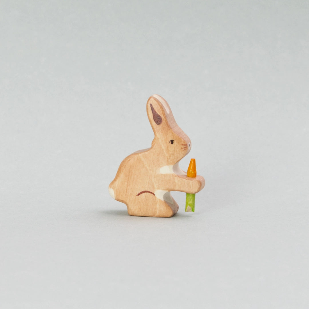 Diese handbemalte Holzfigur „Hase mit Karotte“ von Holztiger zeigt ein niedliches Holztier mit hellbraunem Fell und weißen Akzenten. Der kleine Hase hält eine leuchtend orangefarbene Karotte mit grünem Stiel fest in seinen Pfoten. Perfekt als liebevolle Holzfigur für Kinder, als Osterdekoration oder für kreatives Spielen.