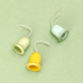 Die drei Glocken der Serie Jingle Joy Bells von den Grapat Ornaments liegen auf einem grünen Untergrund. Die Weihnachtsbaumanhänger sind aus Holz gefertigt und in Gelb, zartem Blau und feinem Grün gestaltet. Sie sind mit Sternen, Sprenkeln und weiteren farblichen Akzenten sowie goldenen Verzierungen geschmückt.