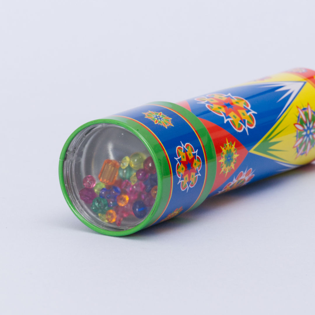 Buntes Kaleidoskop aus Metall mit Drehmechanismus von der Marke Goki. Das bunte Metallrohr ist liegend zu sehen und die farbenfrohen Perlen sind an einem der flachen Enden des Zylinders eingeschlossen. Diese können sich frei bewegen damit, wenn man das Ende des Rohres dreht, immer wieder neue Muster und Farbkombinationen entstehen.