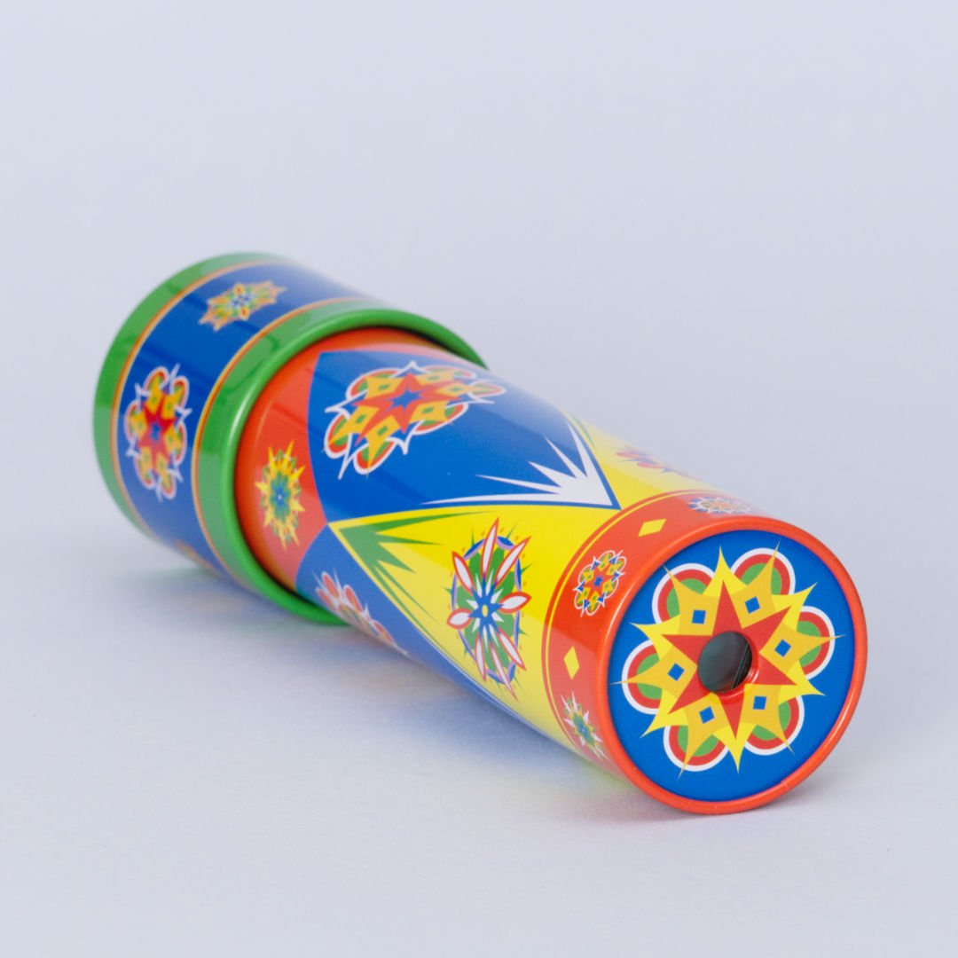 Buntes Kaleidoskop aus Metall mit Drehmechanismus von der Marke Goki. Das bunte Metallrohr ist liegend zu sehen und das Guckloch ist auf flachen Seite des Zylinders umrahmt von einem bunten Muster, welches dem Effekt im Kaleidoskop ähnelt. Weitere rundliche Mandala Formen mit geometrischen Elementen sind auf dem ganzen Rohr verteilt. Enthaltene Farben sind Grün, Rot, Gelb, Blau, Orange und Weiß.