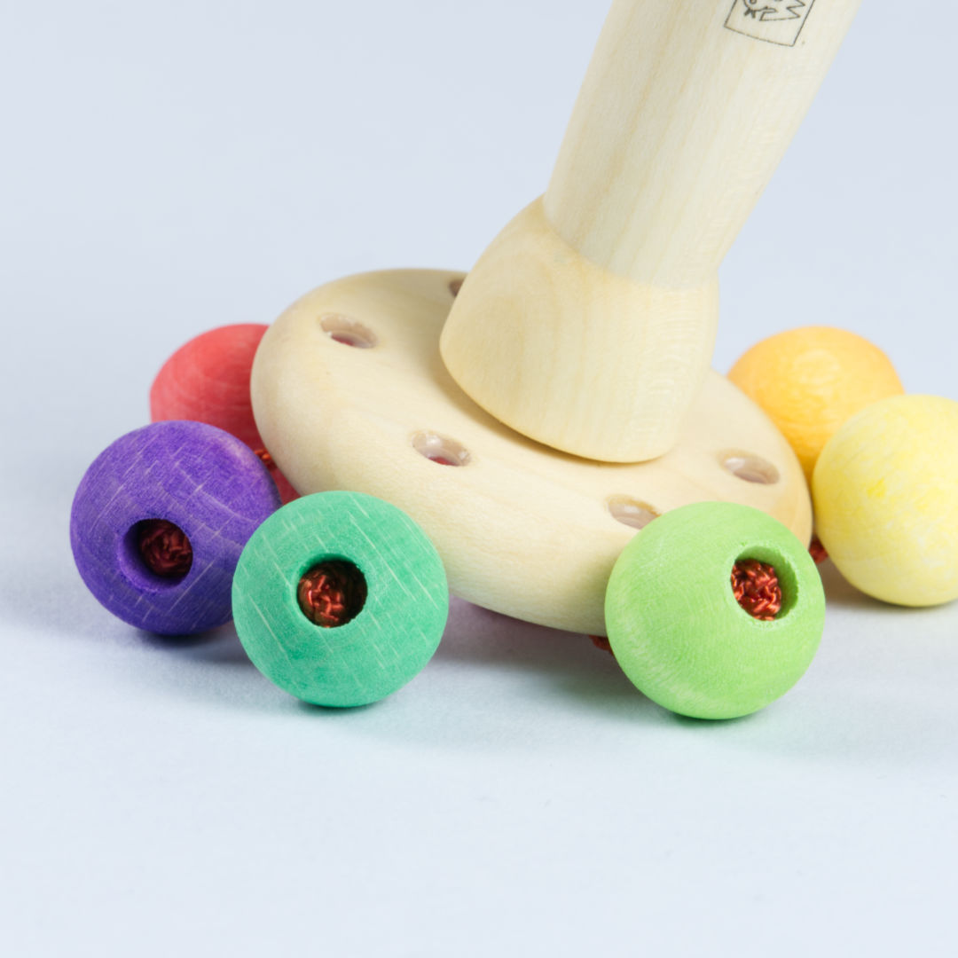 Detail, Karussell Rassel, rote Schnur befestigt bunte Holzkugeln an Rasselkopf.