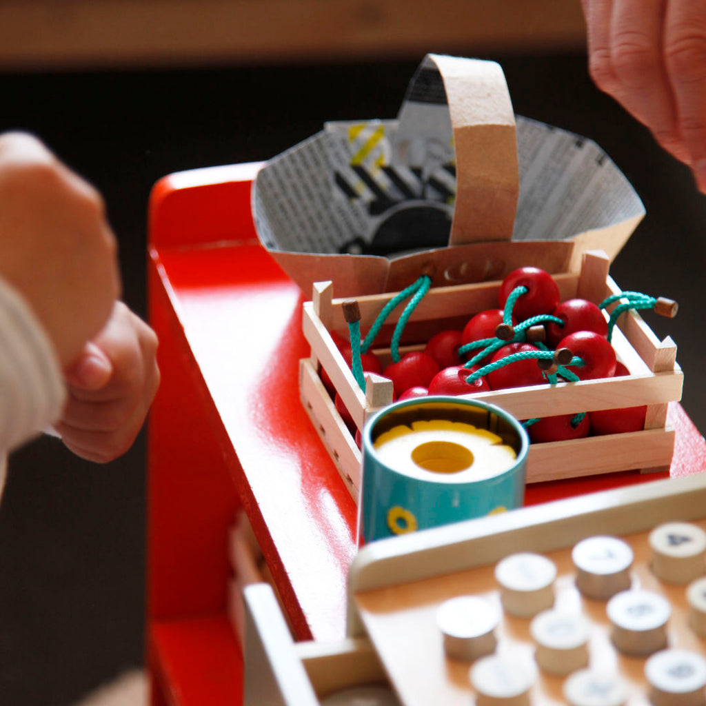 Im Mittelpunkt spiel Obststiege gefüllt mit spiel Kirschen aus Holz. Dahinter DIY Körbchen aus einem alten Milchkarton.
