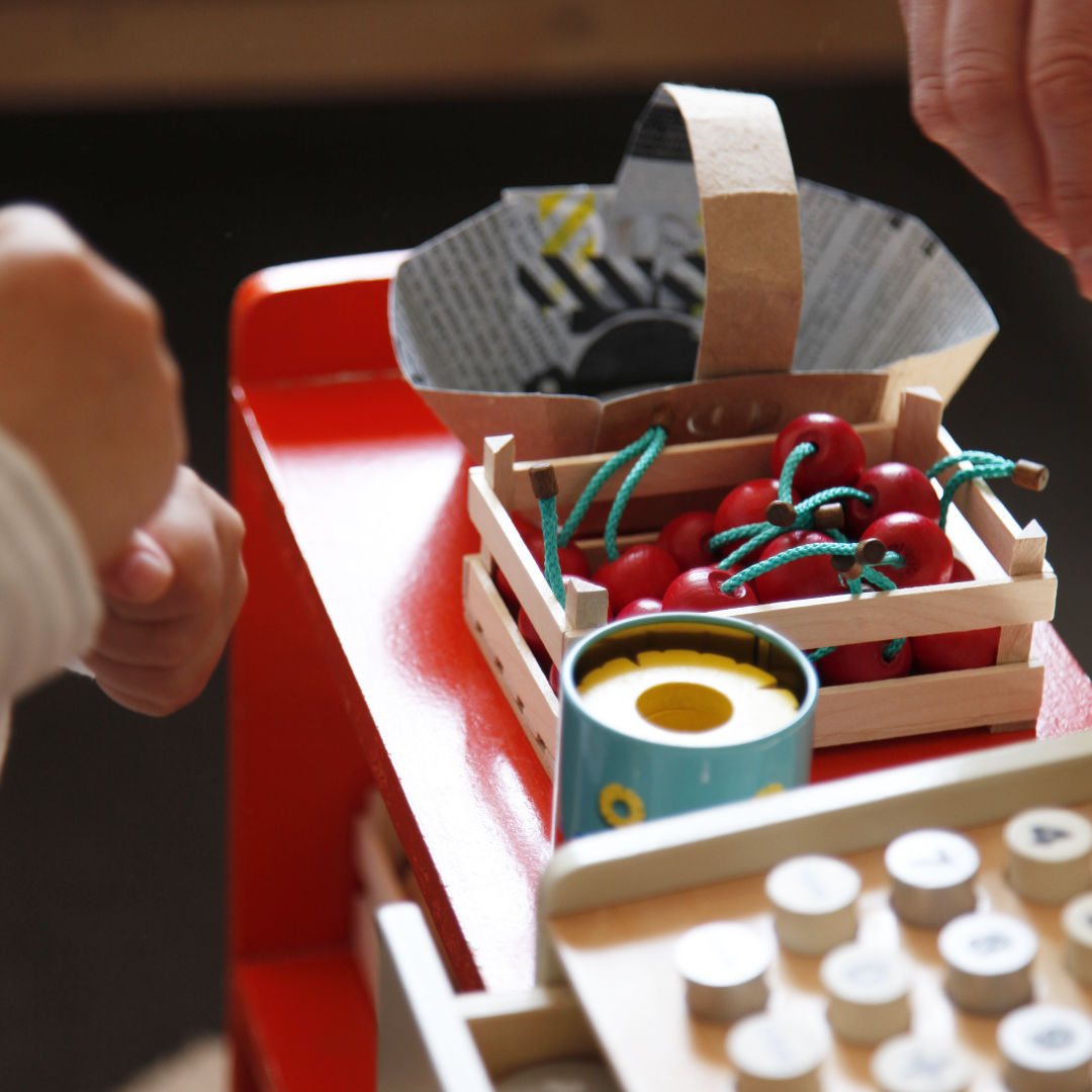 Im Mittelpunkt spiel Obststiege gefüllt mit spiel Kirschen aus Holz. Dahinter DIY Körbchen aus einem alten Milchkarton.