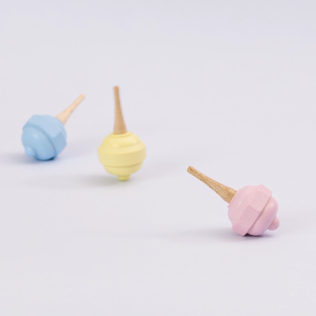 Pastellkreisel in rosa aus Holz von Beck. Seitenansicht. im Hintergrund der gelbe Kreisel drehend und der blaue Kreisel liegend.