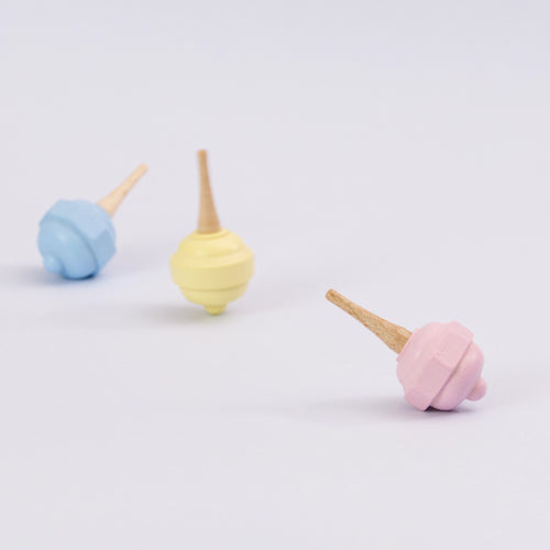 Pastellkreisel in rosa aus Holz von Beck. Seitenansicht. im Hintergrund der gelbe Kreisel drehend und der blaue Kreisel liegend.