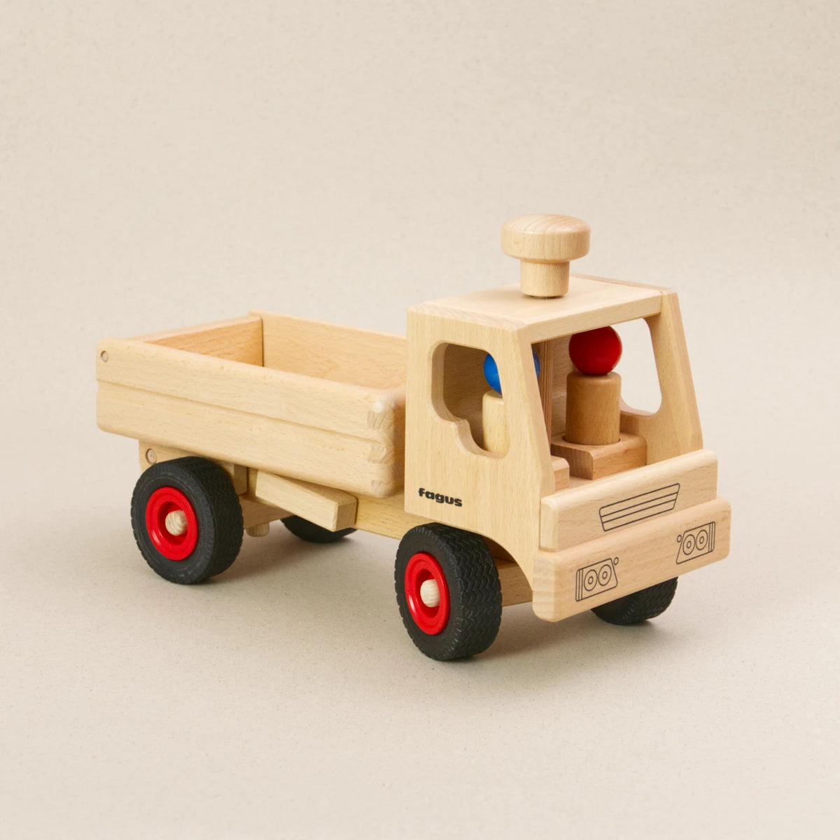 Holzfahrzeug LKW Kipper von fagus aus naturlackiertem Buchenholz mit Vollgummireifen und großer Ladefläche. Ansicht von Vorne links, in der Fahrerkabine sitzen zwei Figuren, auf dem Dach ist ein Lenkknopf.