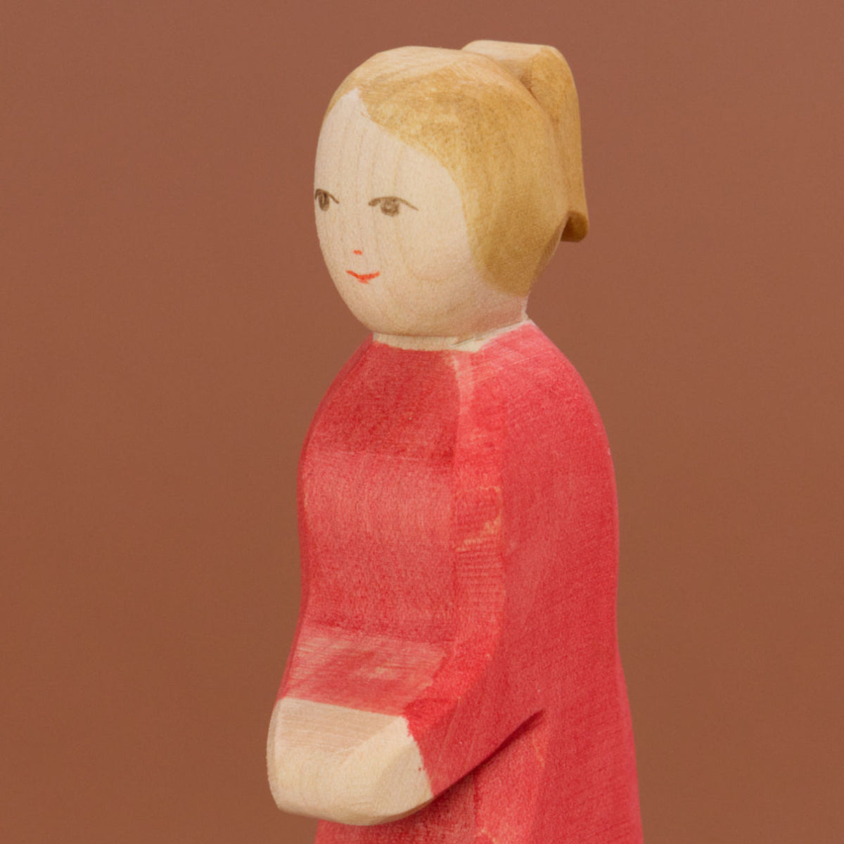Die Holzfigur Mutter von der Marke Ostheimer ist in einer Nahaufnahme, ähnlich wie in einem Porträt, zu sehen. Sie hat eine heller Hautfarbe, ihre blonden Haare sind zu einem Pferdeschwanz zusammengebunden und sie trägt ein intensiv rosa Kleid.